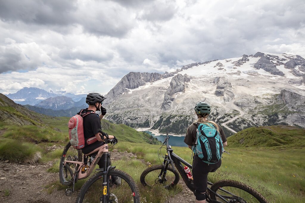 Bike Marmolada Persone che vanno in bike di fronte al Lago di Fedaia e la Marmolada in Val di Fassa