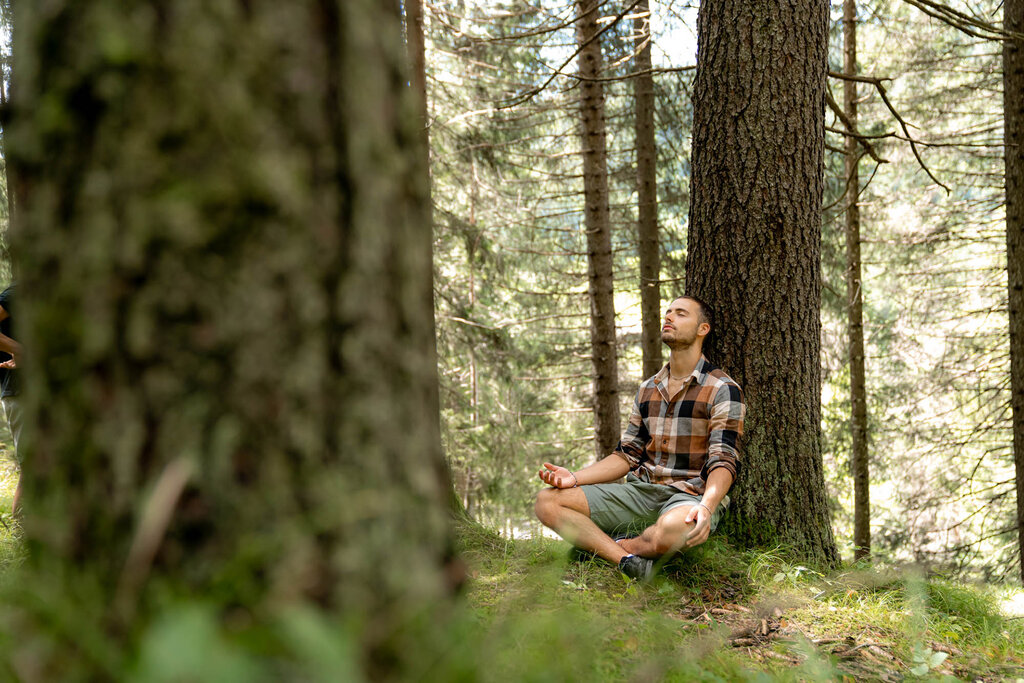 Benessere nei boschi della Val di Fassa Un uomo medita seduto sotto ad un albero