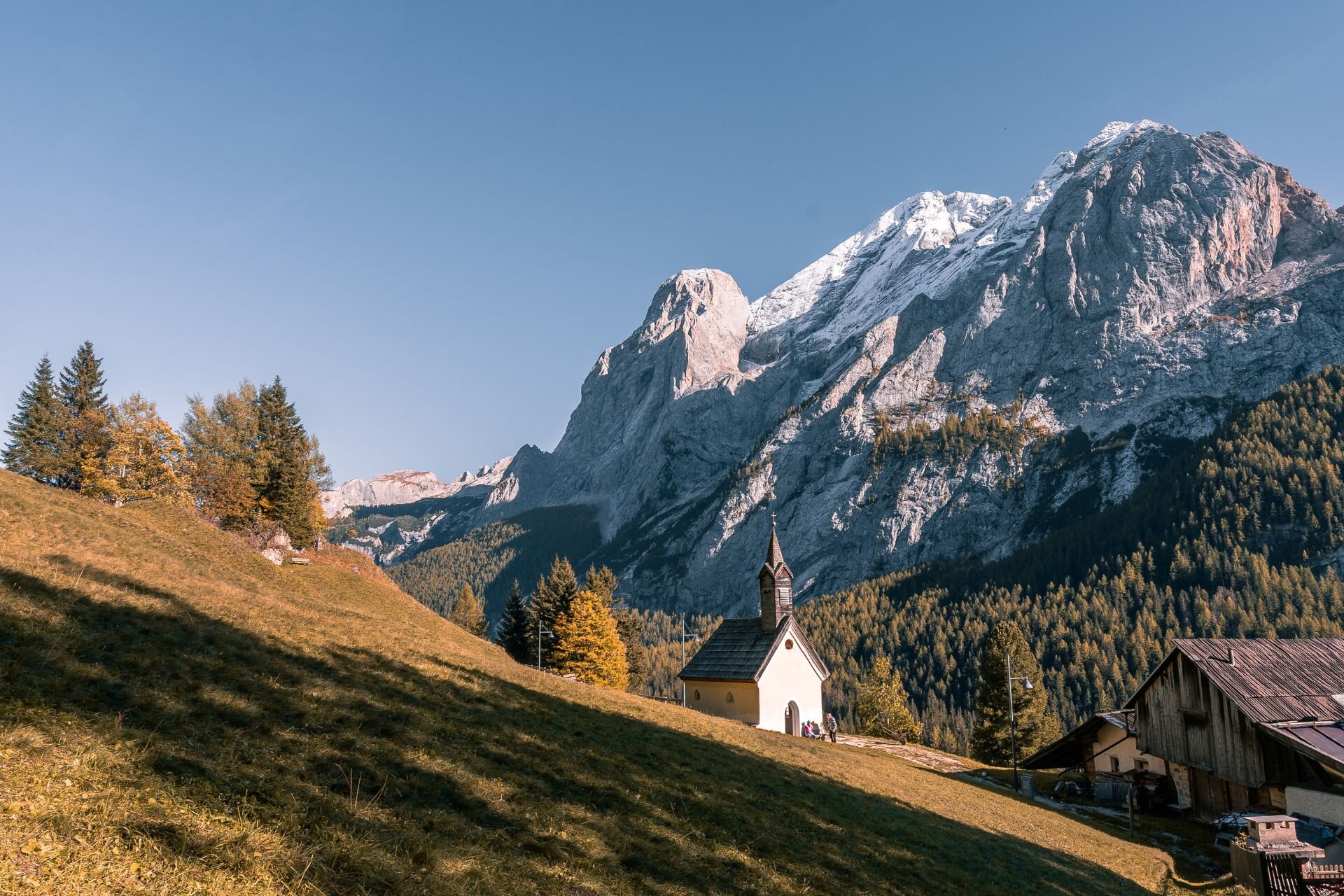La chiesetta di Penia di fronte alla Marmolada | © Archivio Immagini ApT Val di Fassa - Patricia Ramirez Chiesetta in mezzo al bosco autunnale con la Marmolada innevata sullo sfondo | © Archivio Immagini ApT Val di Fassa - Patricia Ramirez